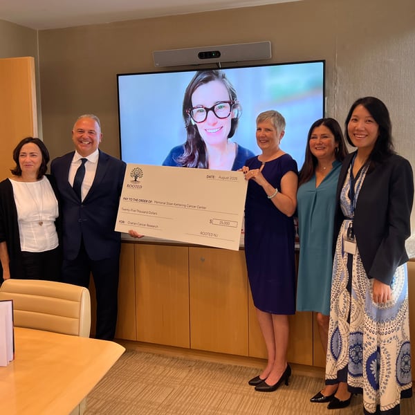Attendees holding a $25,000 ceremonial check beneath a video-call display, with I Hope You Know on the table.